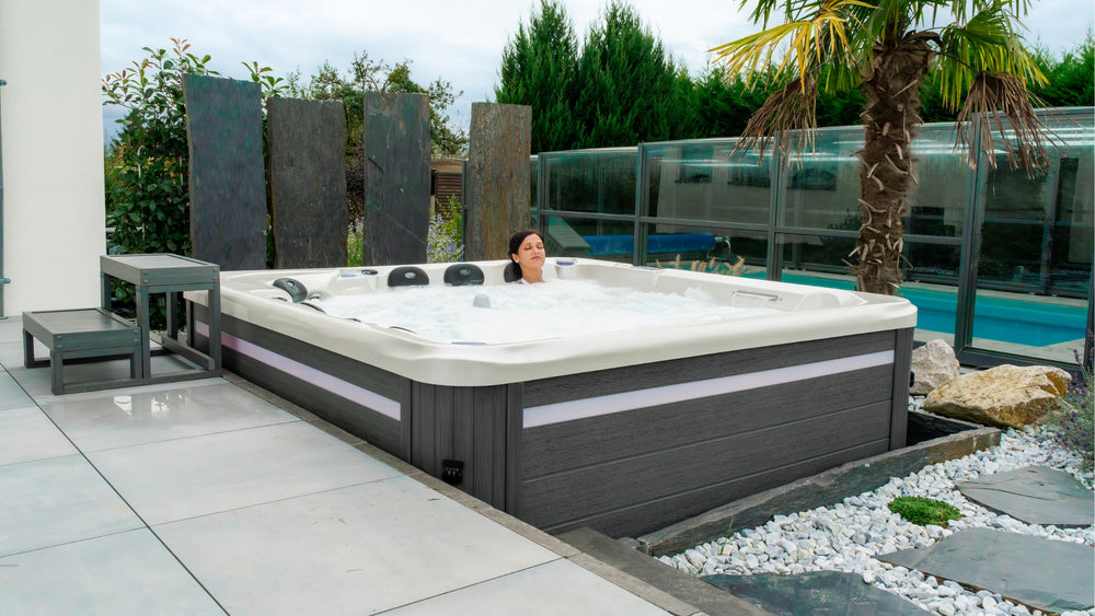 Image d'un Spa Bora Bora de la marque ZigZag SPA installé prêt d'une piscine avec une femme qui profite du massage